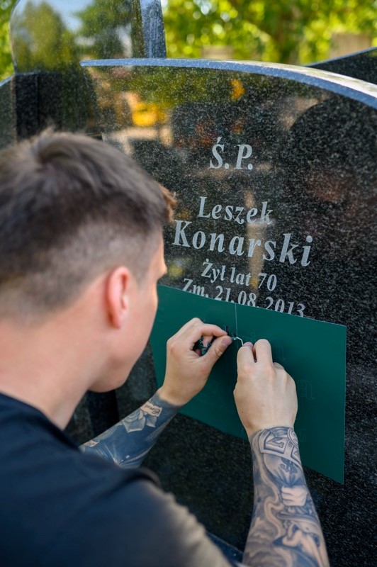 Wojciech Grabowski wykonuje napis na nagrobku z zielonym szablonem